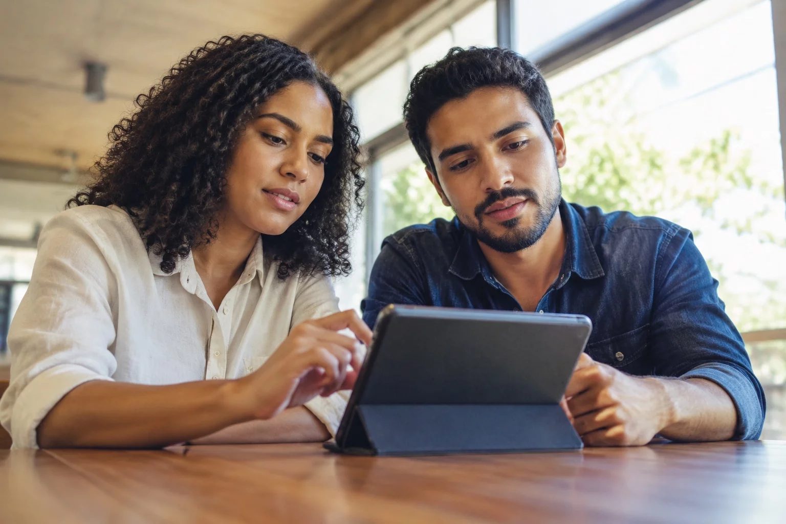 Duas pessoas revisando anotações em um tablet sobre uma mesa de madeira